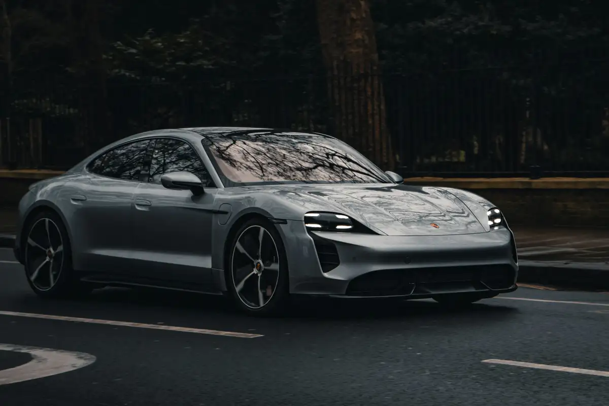 A silver car driving down a street next to a forest